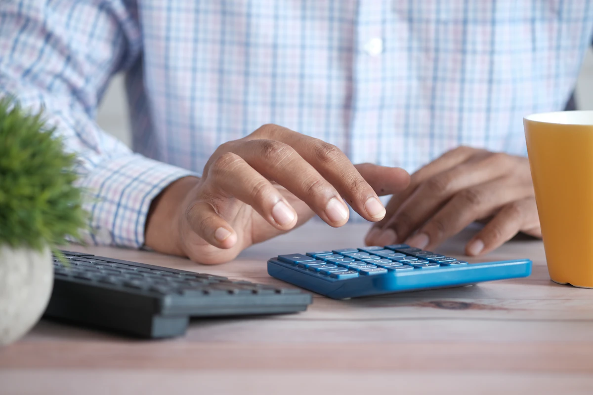 Mani che usano una calcolatrice sulla scrivania accanto alla tastiera