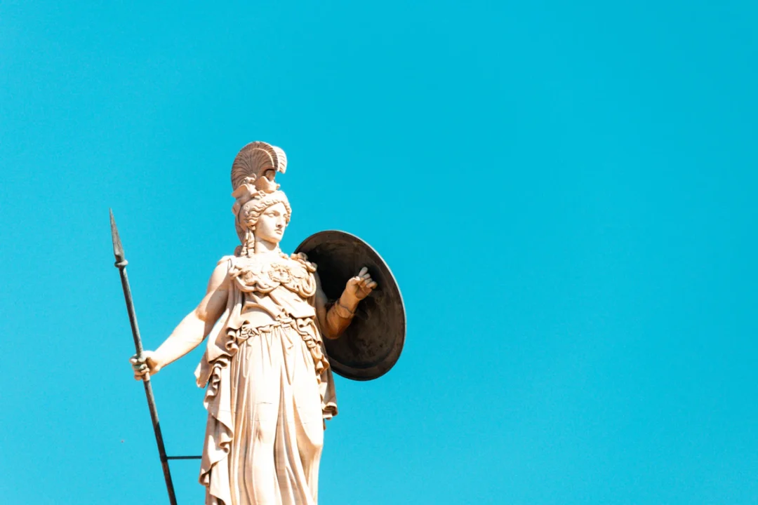 Statua di una dea armata con elmo, lancia e scudo contro il cielo azzurro, iconografia di Atena
