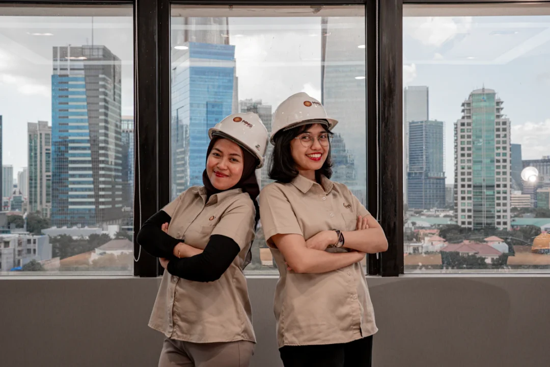 Due donne con elmetto e divisa da lavoro in un ufficio con vista sulla città